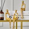 Three gold abstract thinker sculptures sitting on a glass desk with stacked books.