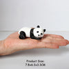 A small white and black panda figurine is held in a person's hand.
