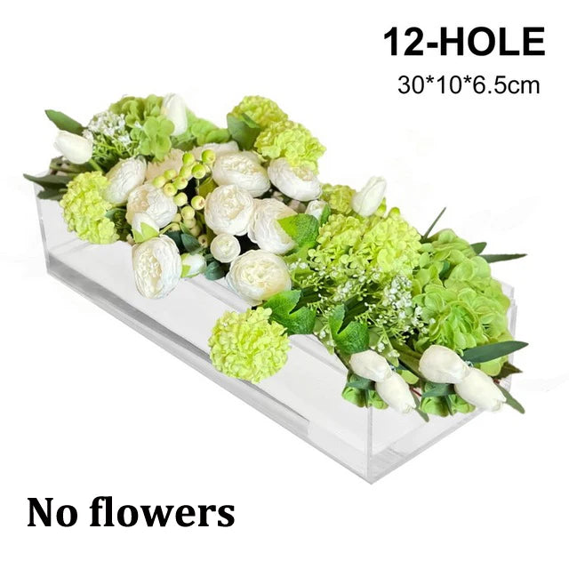 A rectangular clear acrylic vase holding a green and white floral arrangement.