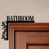 A dark metal bathroom door sign with the word BATHROOM mounted on a wooden frame.