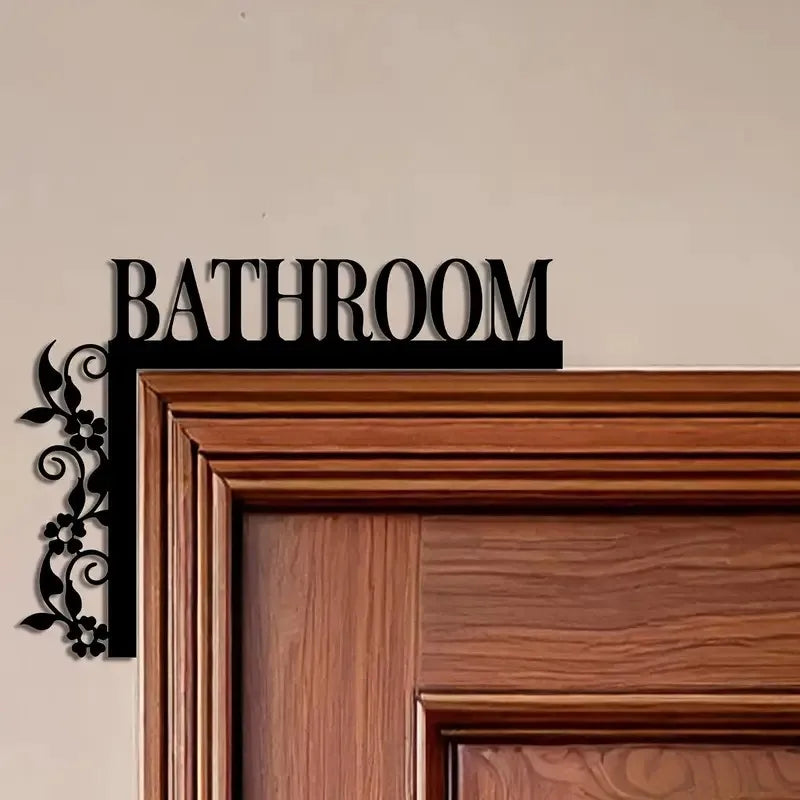 A dark metal bathroom door sign with the word BATHROOM mounted on a wooden frame.