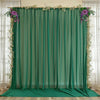 A sheer green chiffon backdrop curtain decorated with purple and white floral greenery for an event or wedding.