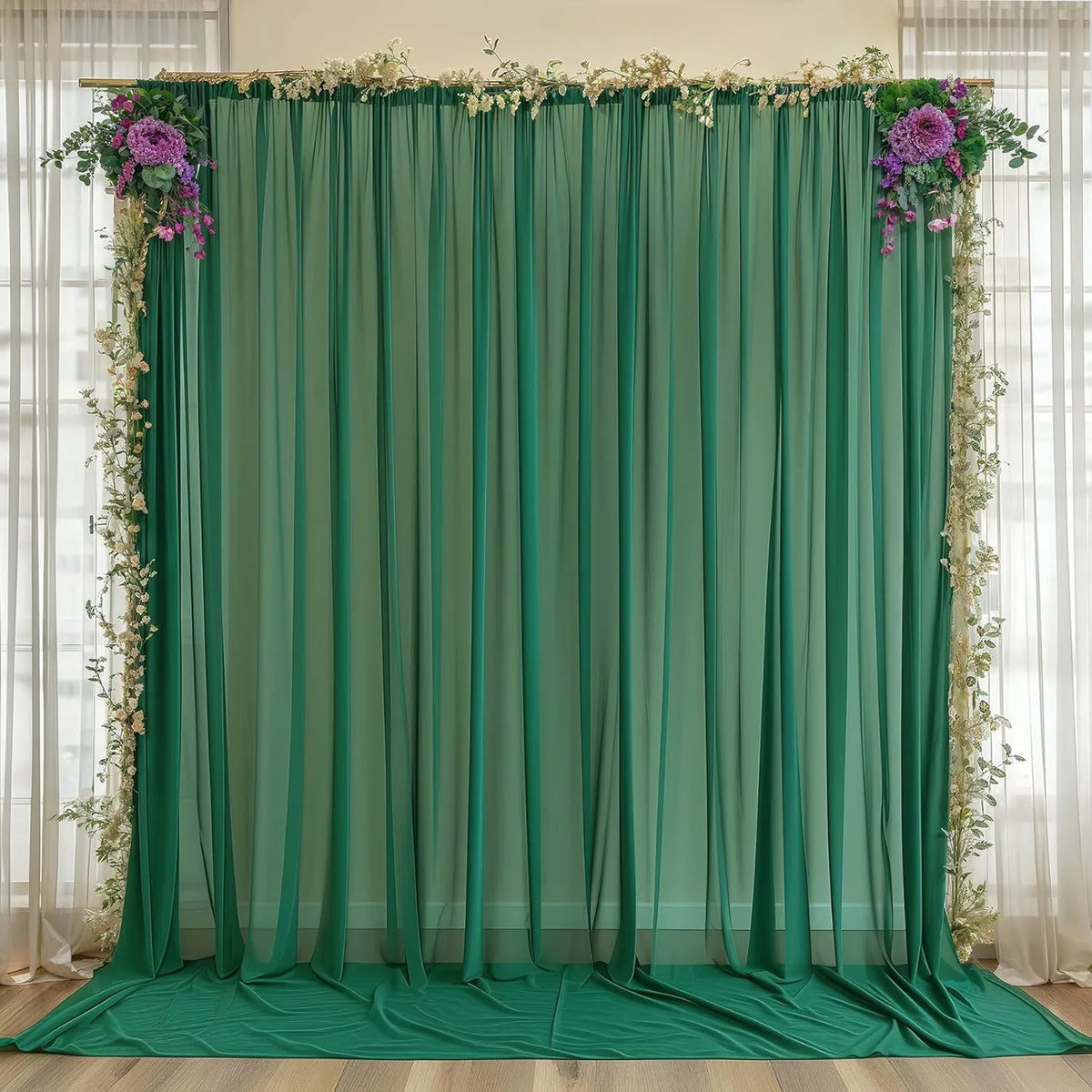 A sheer green chiffon backdrop curtain decorated with purple and white floral greenery for an event or wedding.