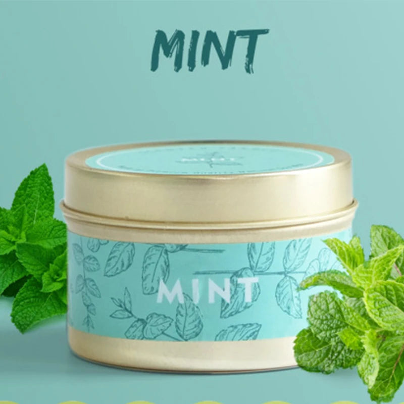 A tin of mint-scented soy wax travel candle with fresh mint leaves surrounding it.