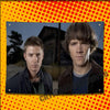 A photo of two men, likely actors or characters, against a dark background with a yellow polka-dot border.