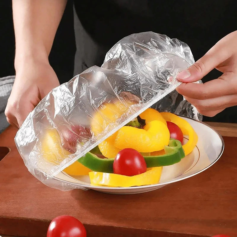 Hands are placing colorful vegetables like bell peppers and tomatoes into a clear reusable plastic food cover.