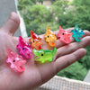 A hand holds several glow-in-the-dark fruit turtle resin charms in various bright colors like orange pink and green.