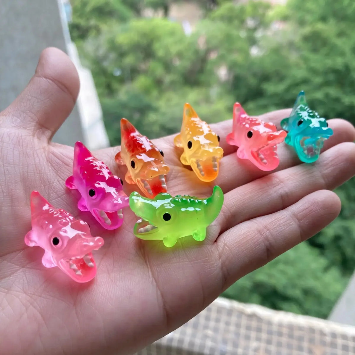 A hand holds several glow-in-the-dark fruit turtle resin charms in various bright colors like orange pink and green.