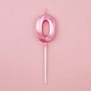 A pink number zero candle on a white stick against a light pink background.