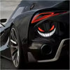 Close-up of a black sports car's headlight with an aggressive red eye design and a silver emblem decal.