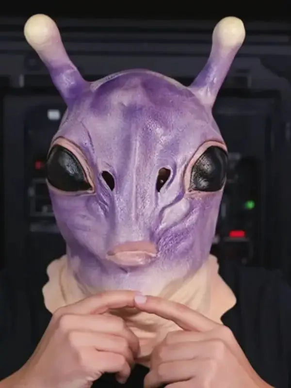 A close-up of a purple alien full-face latex mask being held by hands.