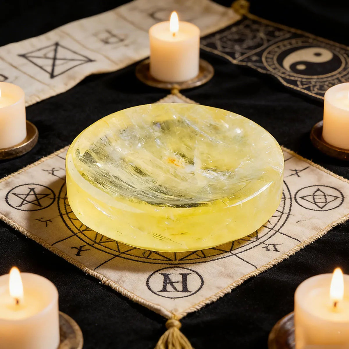 A round, translucent yellow citrine crystal bowl sits on a lace cloth surrounded by lit candles.