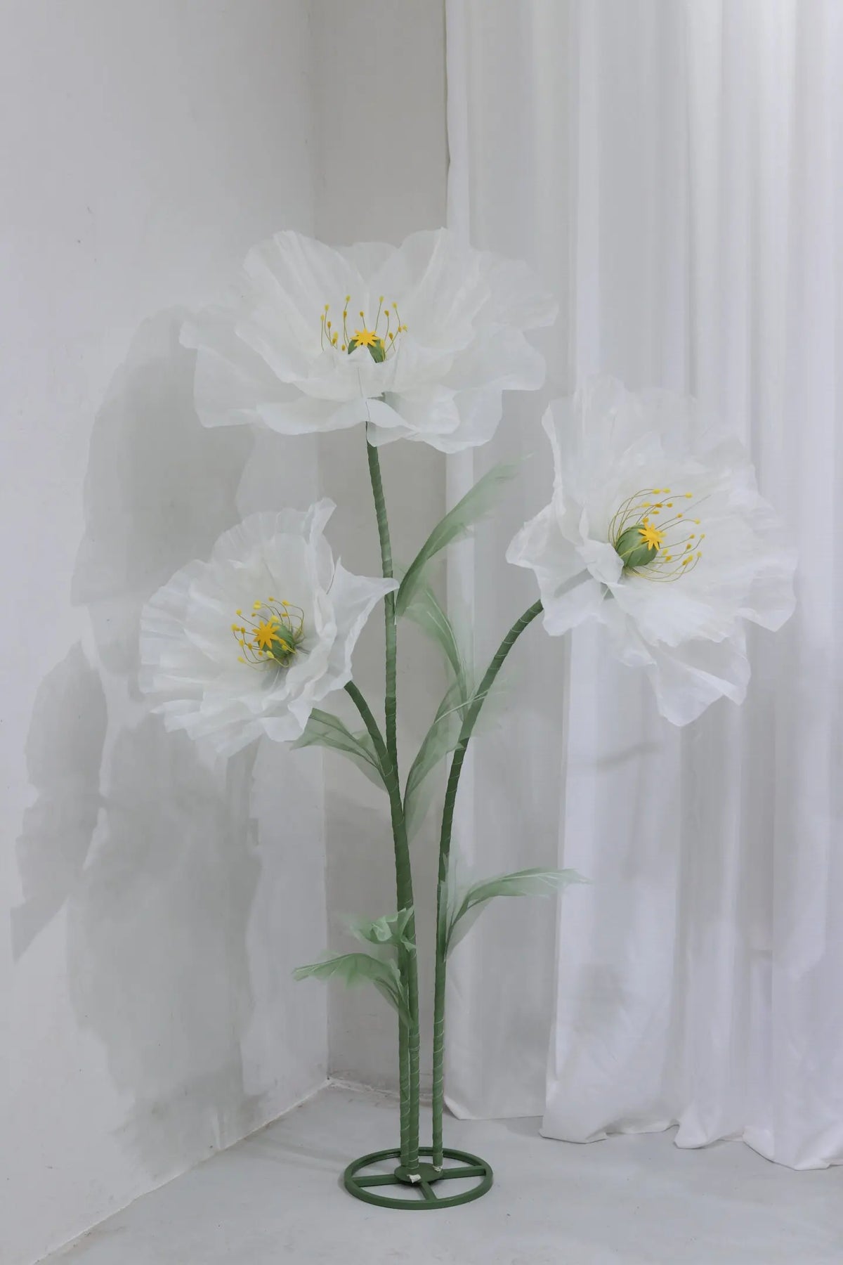 A large artificial silk white poppy flower displayed on a green stand against a white background.