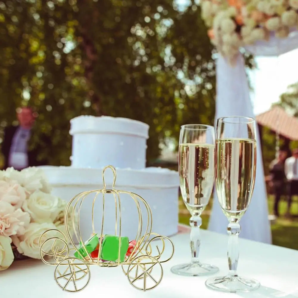 A golden pumpkin carriage candy box displayed on a white table with champagne glasses and floral arrangements.