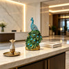 An elegant blue peacock statue with a crystal tail feathers displayed on a marble countertop.