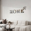 Decorative wall decal spelling the word HOME in silver letters with a butterfly accent on a white wall above a sofa.