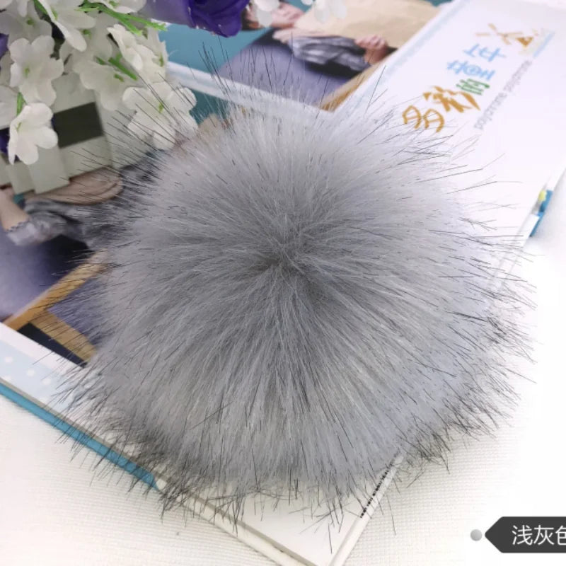Pompon en fausse fourrure grise sphérique posé sur un livre.
