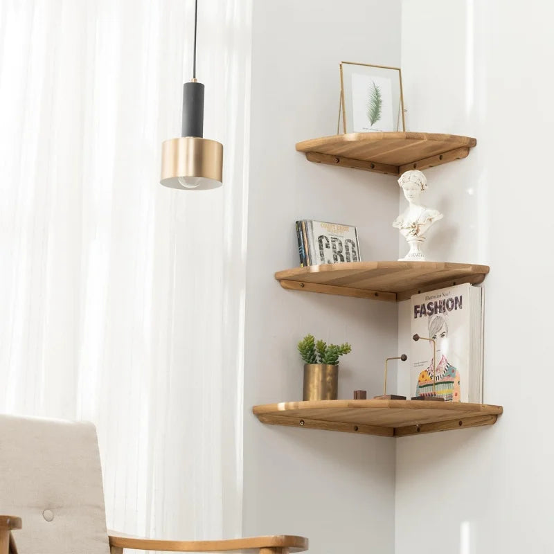 A natural wooden corner floating shelf mounted on a white wall with decorative items and a pendant light.