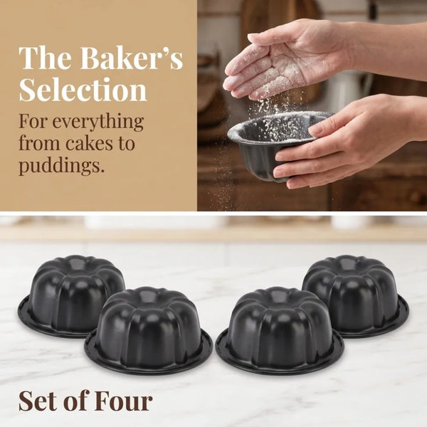 A set of four black nonstick mini fluted cake pans being held by a hand, with baking ingredients visible in the background.
