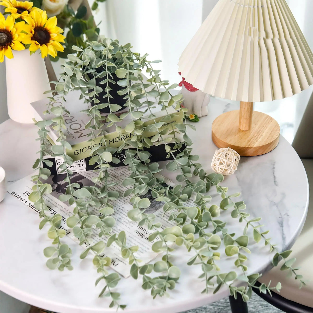Plantes d'eucalyptus artificielles suspendues sur une table blanche à côté d'une lampe de couleur crème.