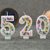 Three glitter number candles 520 decorated with colorful candy beads on a gray fabric background