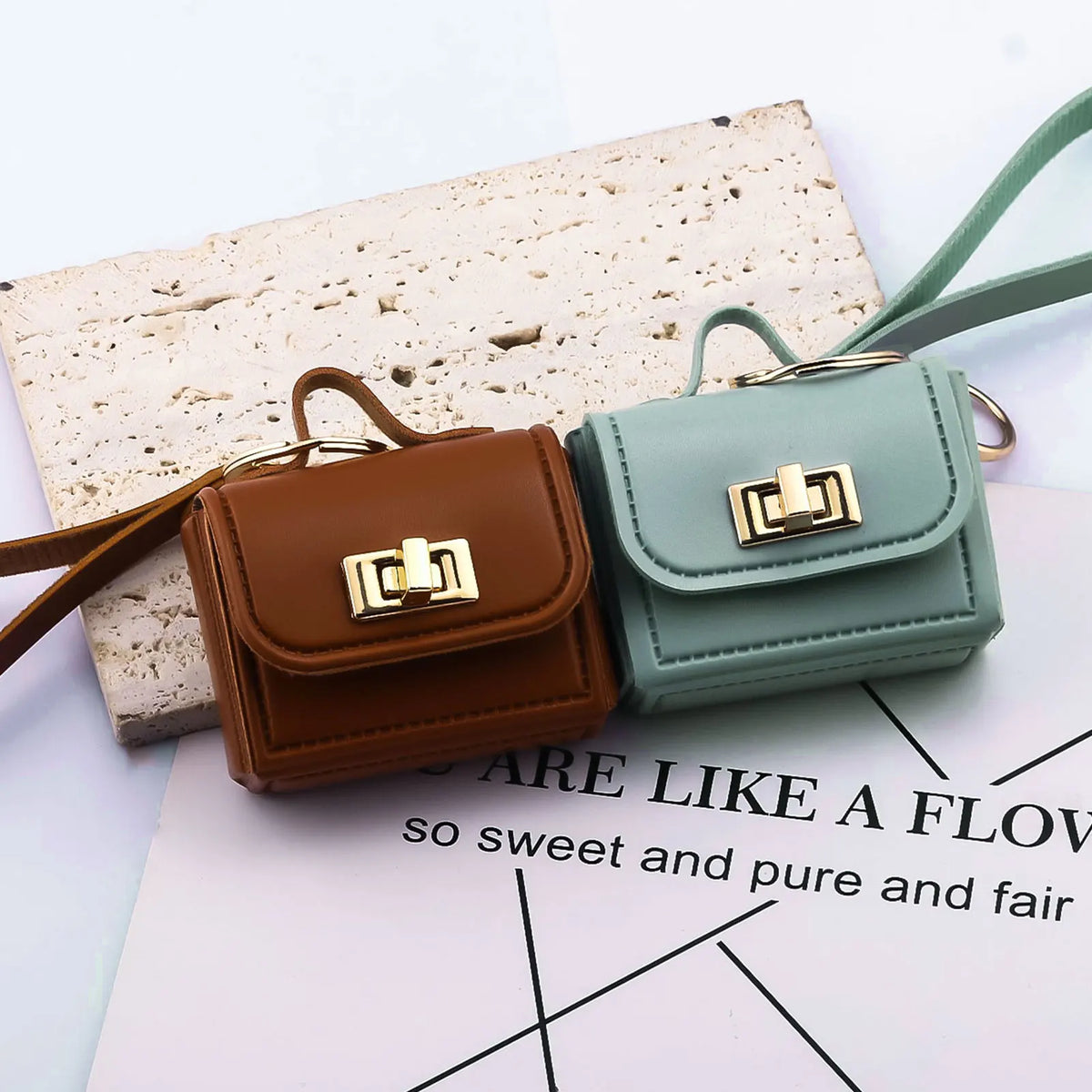 A pair of mini leather openable bags in brown and mint green colors resting on a white paper background.
