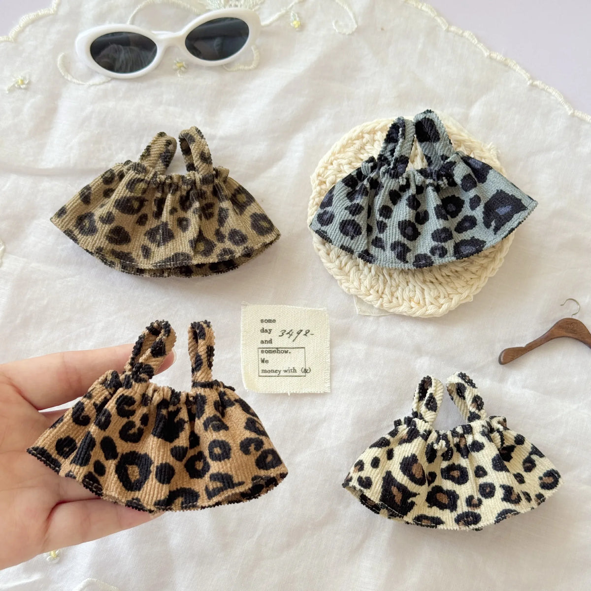 Three leopard print shoulder strap skirts for dolls displayed on a white cloth.