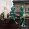 A resin statue of a green alien sitting on a rock, holding a glass of beer.