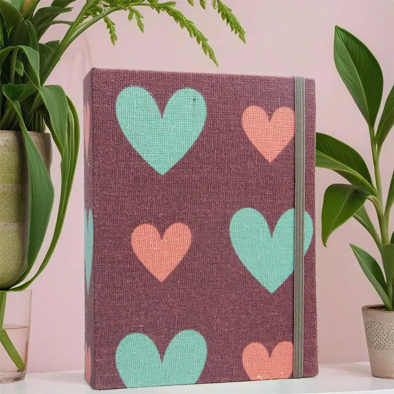 Hartcover-Fotoalbum mit strukturiertem lila Einband und wiederkehrenden hellgrünen und pfirsichfarbenen Herzformen.