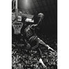 Black and white photo of a basketball player dunking during a game against a dark background.