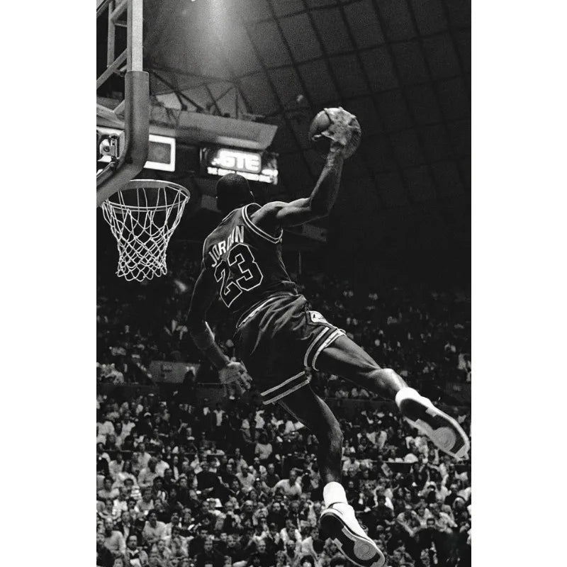 Black and white photo of a basketball player dunking during a game against a dark background.