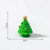 A small, bright green resin Christmas tree charm with a gold star topper resting on white snow.