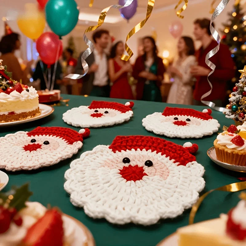 A set of handmade crochet Santa Claus coasters with red and white yarn displayed on a green surface.