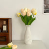 A white ceramic bud vase holds a bouquet of pale yellow and cream tulips.