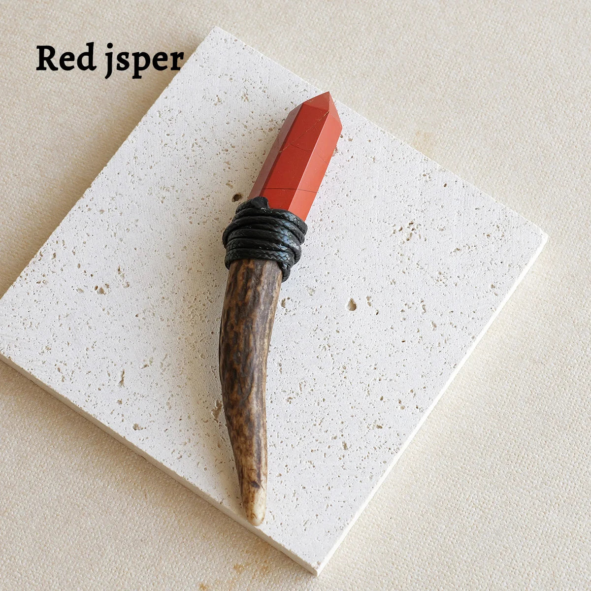 A reddish-orange crystal scepter wand with a dark handle rests on a white square surface.