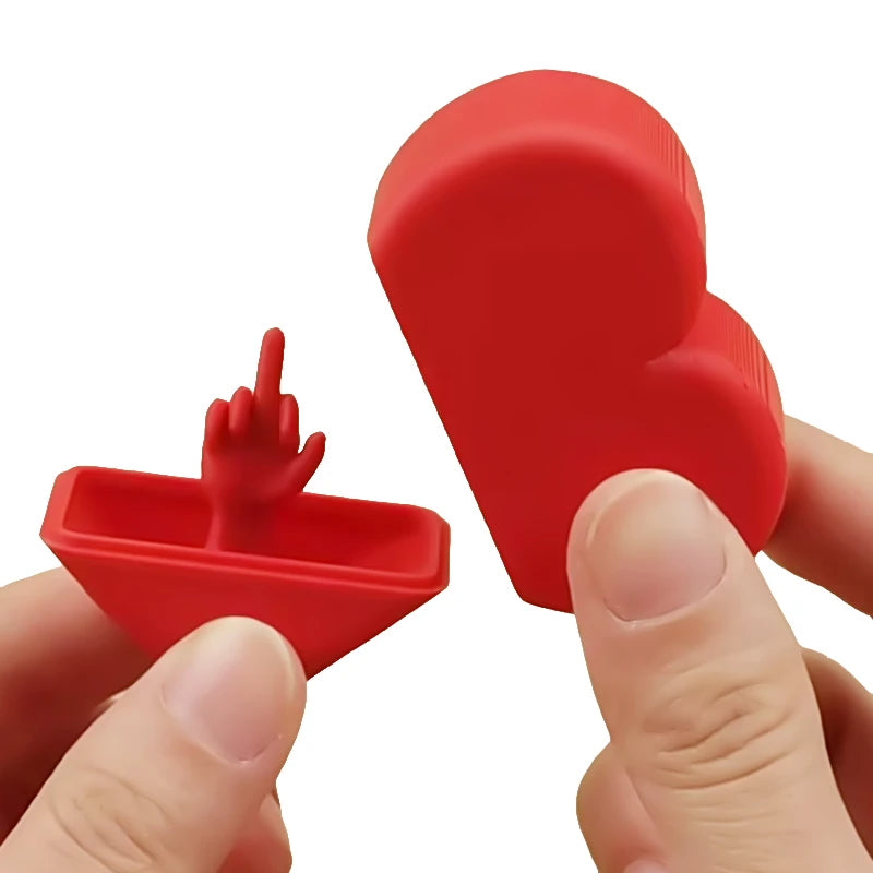 A hand holds a red, heart-shaped novelty desk decor item with a finger gesture.