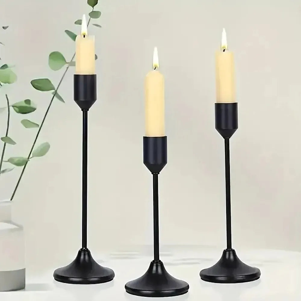 A set of three black minimalist retro tabletop candle holders with white taper candles on a white surface.
