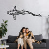 A couple sits on a dark sofa in front of a white brick wall featuring a black line sculpture of a shark swimming.