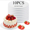 A white frosted cake is displayed in front of a stack of round cake boards, with fresh strawberries and berries around the ba
