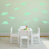 A white wooden dining set with light green glow in the dark dinosaur wall decals on a pale green wall.