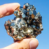 A hand holds a cluster of sparkling natural pyrite crystals against a clear blue sky.