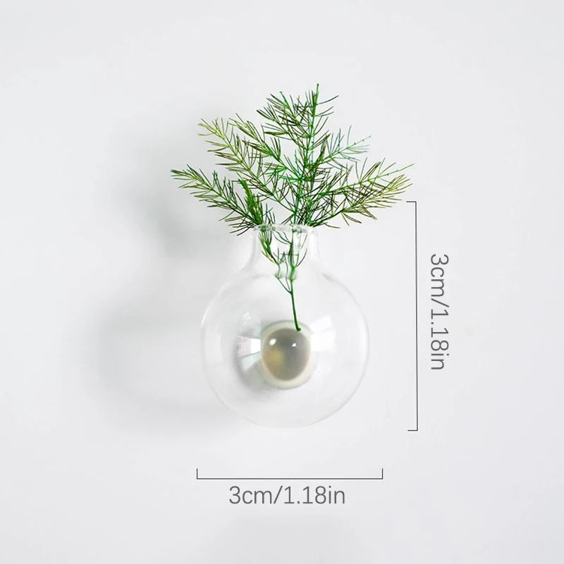 A clear glass vase holds a sprig of green foliage, used as a decorative item.