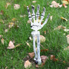 A white realistic skeleton arm stake used for Halloween lawn decor is placed in green grass with fallen leaves.