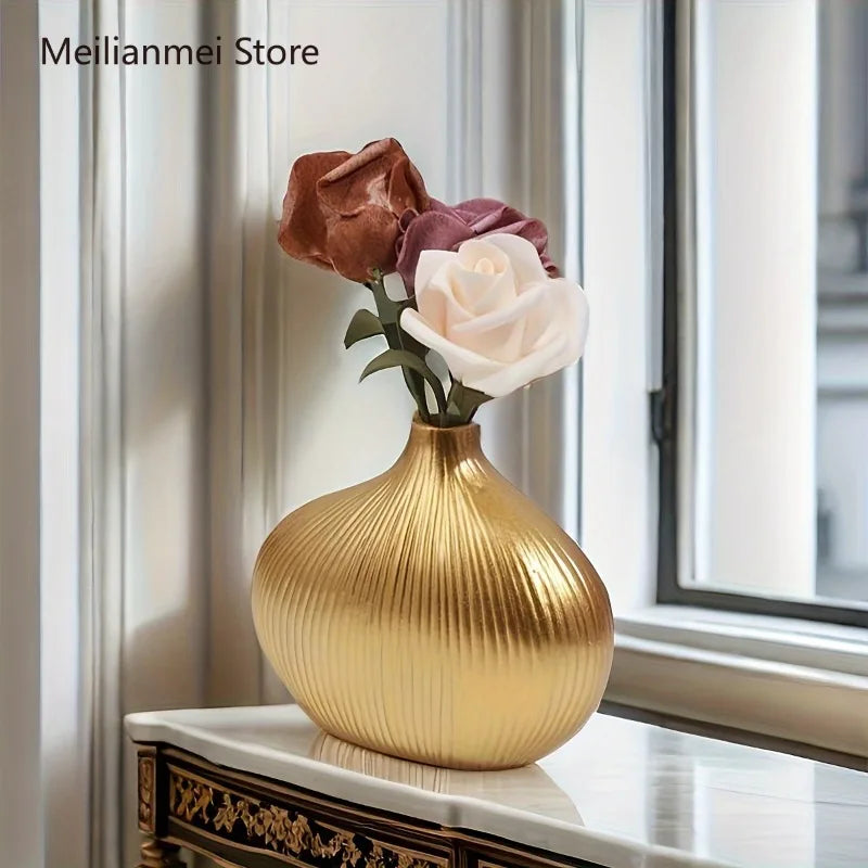 A golden, vertically striped resin vase holding a pink rose in a bright interior setting.