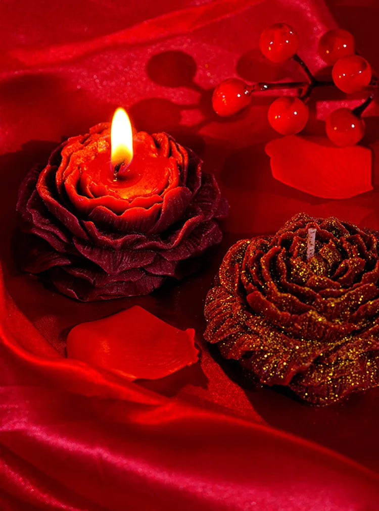 Nahaufnahme einer roten Kerze und einer glitzernden rosenförmigen Kerze auf rohem Seidenstoff.