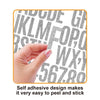 A hand is peeling and sticking glitter alphabet letter stickers onto a surface.
