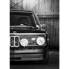 Ein schwarzes Vintage-Auto in Nahaufnahme, frontal aufgenommen vor einer Wellblech-Hintergrund.