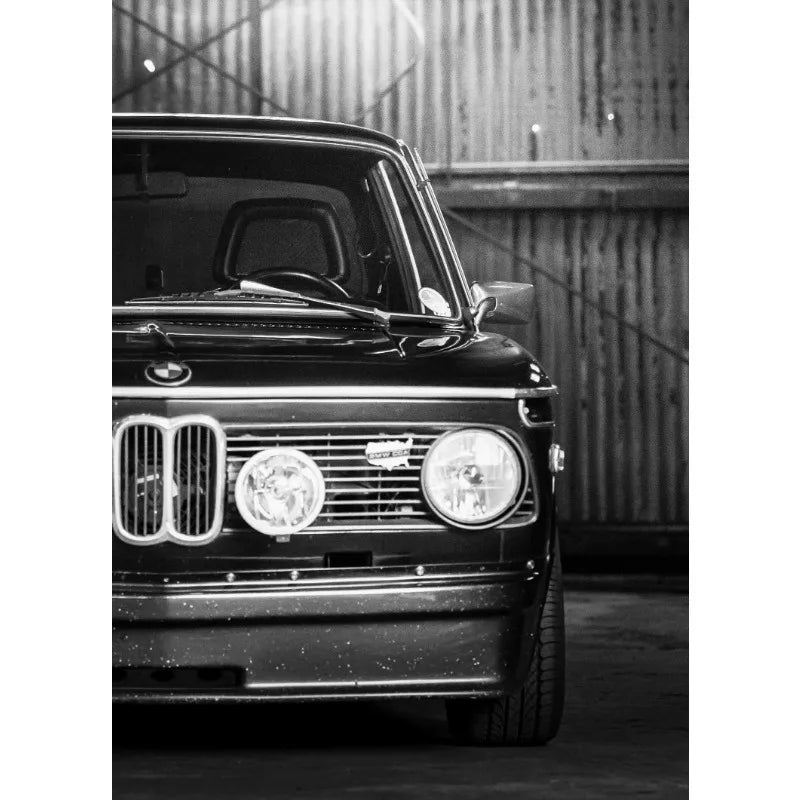 Ein schwarzes Vintage-Auto in Nahaufnahme, frontal aufgenommen vor einer Wellblech-Hintergrund.