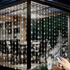 A hand holds a remote control illuminating fairy lights draped across a glass window, creating a sparkling effect.