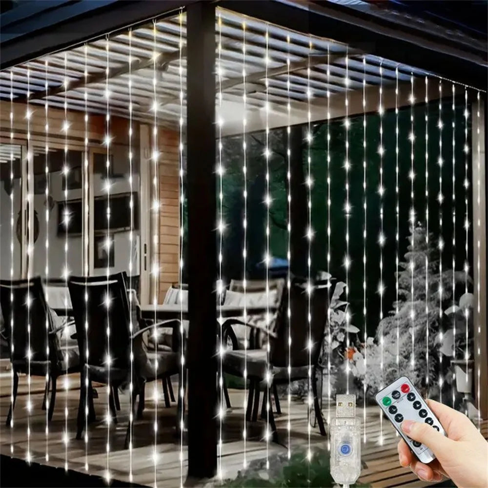 A hand holds a remote control illuminating fairy lights draped across a glass window, creating a sparkling effect.